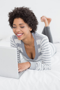 微笑的年轻女子在床上使用笔记本电脑