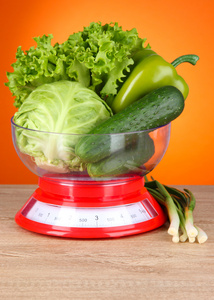 新鲜蔬菜在体重秤上橙色背景表格