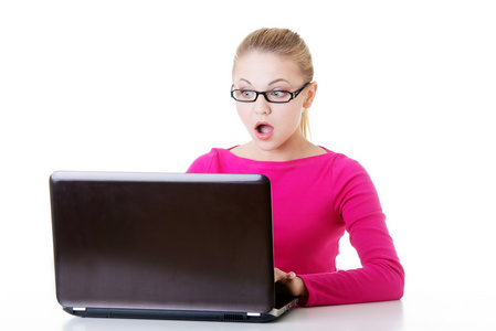 年轻吃惊女人坐在笔记本电脑前