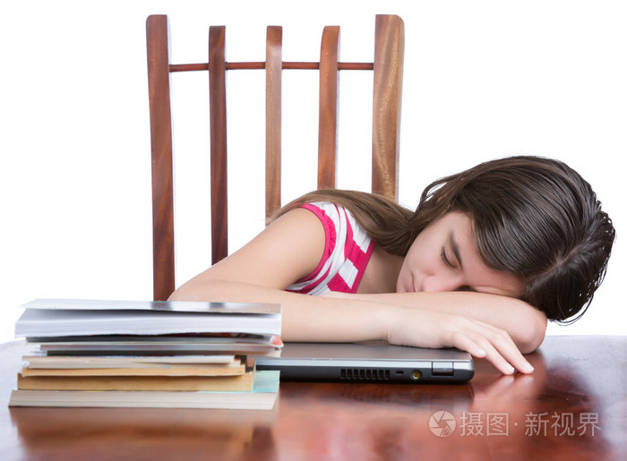 疲倦的女孩在她的便携式笔记本电脑一摞书在桌子上睡着