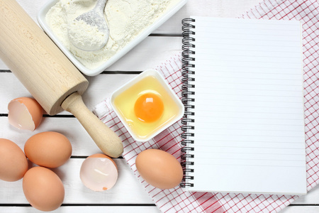 笔记本 鸡蛋 面粉和擀面杖木制的桌子上