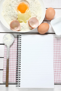 笔记本 鸡蛋 面粉和勺子木制的桌子上