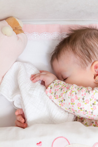 宝贝女孩睡在一张小床与婴儿奶嘴和玩具
