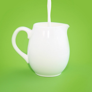 牛奶浇在绿色背景上的白色水罐