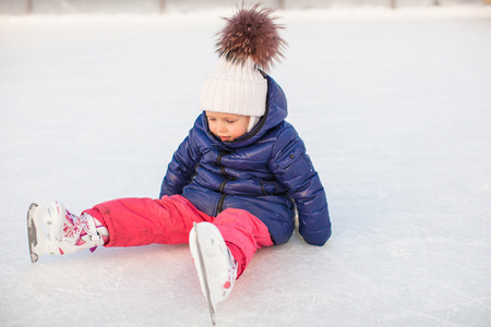 跌倒后坐在冰上滑冰鞋上的小可爱女孩