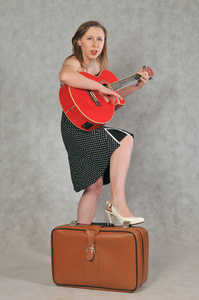 一个快乐的女孩, 带着一把红色的吉他和一个复古的手提箱