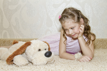 小女孩带着毛绒狗躺在地毯上