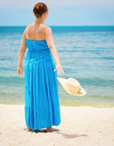蓝裙子的女人在海滩上引发的帽子
