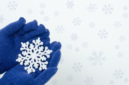 紧靠双手戴上蓝色手套，拿着一大朵的雪花。连指手套和雪花在洁白的雪地背景上