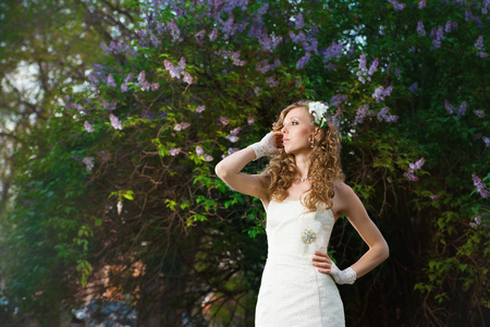 美丽的新娘穿着白色连衣裙在春天中的淡紫色背景上
