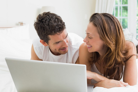 微笑着对夫妇在床上使用笔记本电脑
