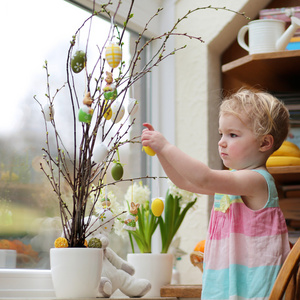 接下来的生活可爱的金发小孩女孩装饰与复活节鸡蛋樱桃树枝接下来站在厨房里一个带有花园的视图窗口照片