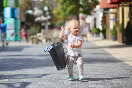 可爱的小宝贝女孩站立或行走在水口村街道中间期间销售提着购物袋黑色，在她手中，人群拥挤的背景