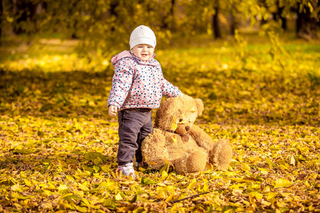 小女孩微笑着在秋天公园举行的泰迪熊