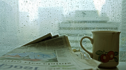 杯咖啡用在黑暗的房间里，外面下着雨的报纸