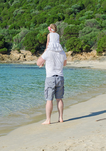 带着女儿在肩膀上站在海滩上的男人