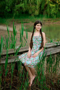 漂亮的女孩坐在森林前面的湖
