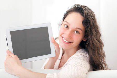 年轻漂亮的女性在沙发上使用平板电脑的肖像
