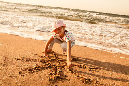 小女孩在沙滩上的沙子上绘制太阳