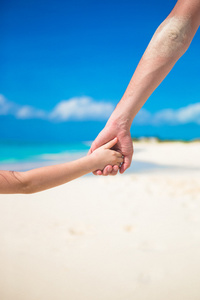 父亲和小女儿在海滩手牵着手互相靠拢
