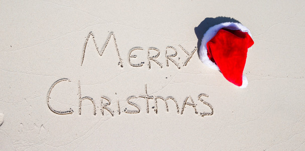 白色的沙滩和圣诞快乐写在沙子上圣诞老人的帽子