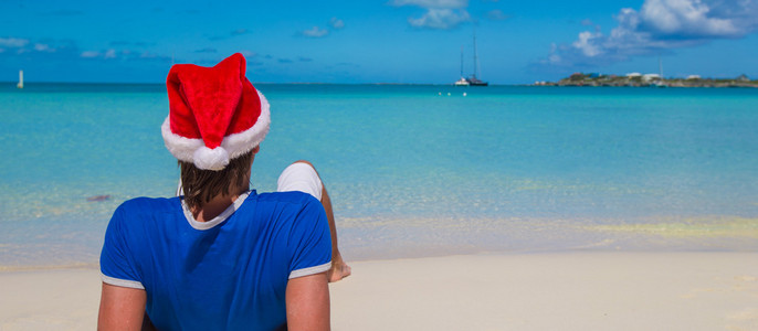 在加勒比的热带海滩回来查看圣诞老人的帽子的年轻人