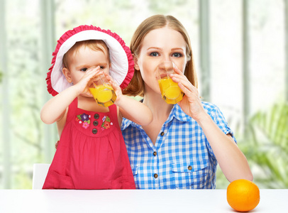 家庭的母亲和宝贝女儿喝橙汁在总和