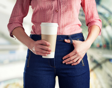 年轻的女人，穿着深蓝色的牛仔裤，拿着一杯咖啡