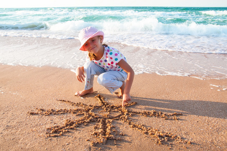 小女孩在沙滩上的沙子上绘制太阳