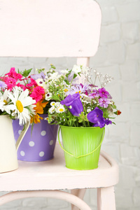 五颜六色的花朵在装饰的水桶，在椅子上，轻质墙体背景上的花束