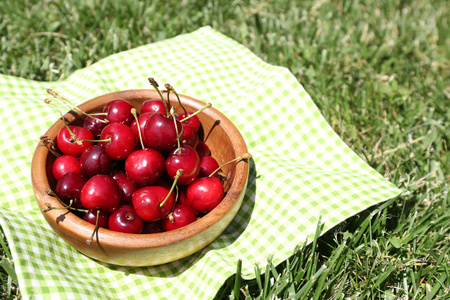 甜甜成熟樱桃的木碗，餐巾，绿草背景