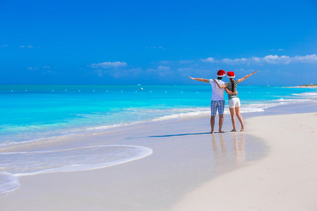 在热带沙滩上回来的红色圣诞帽的年轻夫妇的视图