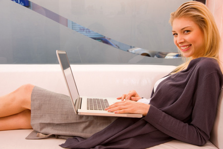 微笑的年轻女士使用笔记本电脑坐在沙发上