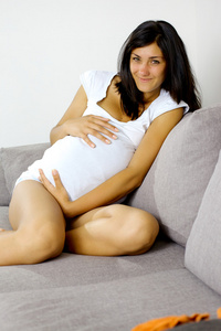 幸福微笑的怀孕女人在家坐在沙发上