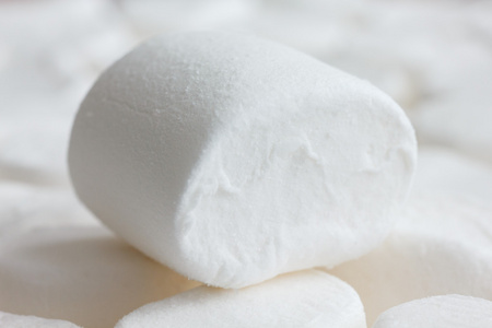 单一的白色棉花糖，坐在其他果汁软糖。模糊的背景
