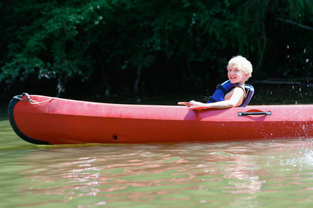 积极快乐十几岁的男孩在河上划独木舟