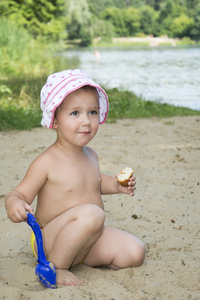 有趣的小女孩坐在湖边的沙滩上在夏天和 s