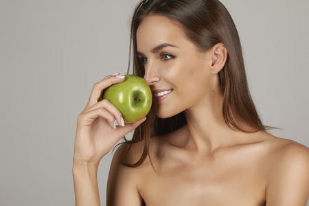年轻漂亮的女孩与黑头发 裸露的肩膀和脖子，拿着大绿色苹果享受品味和在节食 健康饮食和天然有机食物，感觉头发洗发水的诱惑