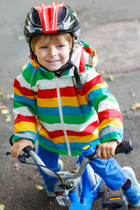 戴红色头盔和五颜六色的雨衣，骑着他的可爱的孩子男孩