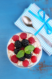 健康酸奶配新鲜水果 浆果和牛奶什锦早餐在玻璃罐中，彩色木背景