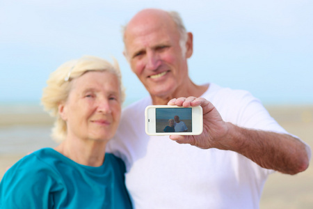 年长的夫妇自手机拍照在沙滩上