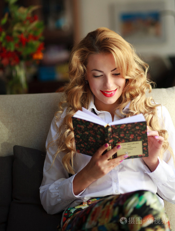 幸福的年轻女人在家里的沙发上读书
