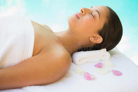 淡定的黑发女人躺在毛巾上，上面有玫瑰花瓣