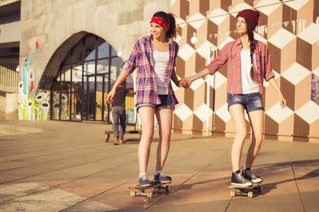 两位黑发少女朋友行家装备 牛仔短裤，keds，格子衬衫，帽子 与滑板在公园户外活动。副本空间