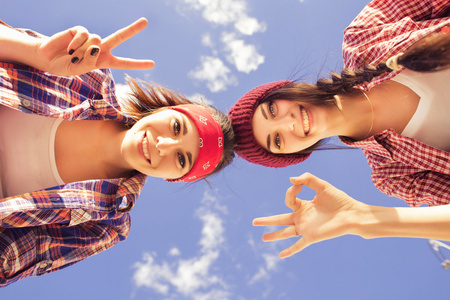 两个黑发少女朋友在行家装备 牛仔短裤，keds，格子衬衫，帽子 与滑板公园户外
