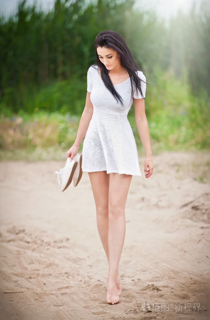 迷人的黑发女孩与短的白色连衣裙,赤脚漫步在乡村的道路上.