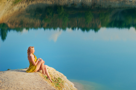 亮妆美丽的女孩坐在岸边的湖，在温暖的夏日海洋