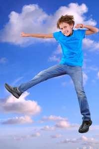 微笑的男孩，跳跃，舞蹈在多云的蓝天