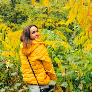 在黄色帽衫走在秋天的树林的可爱女人