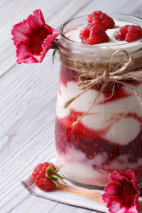 美味的覆盆子酸奶在一个玻璃罐特写和鲜花